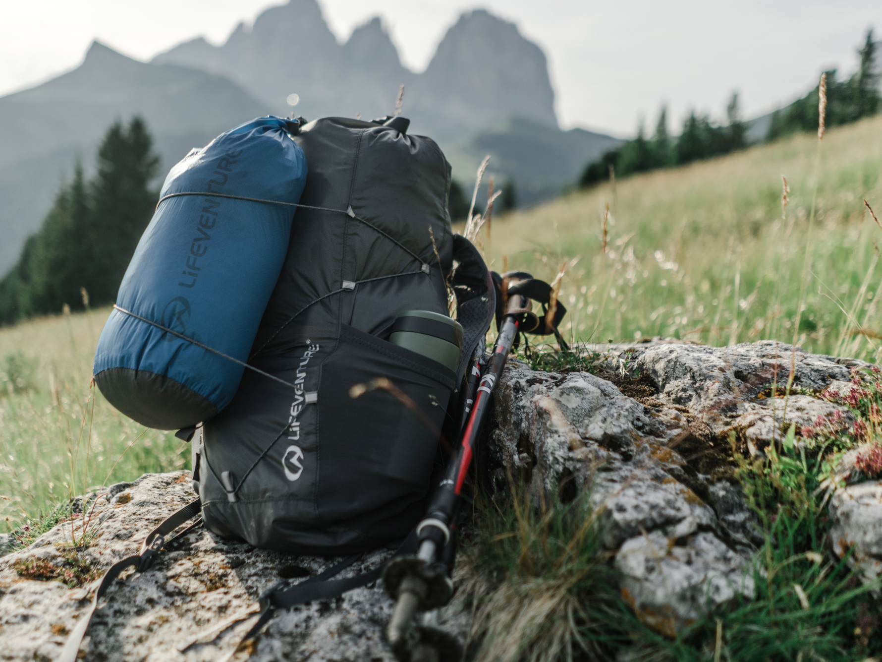 Lifeventure backpack and dry bags with trekking poles resting on a rock during a remote mountain hike